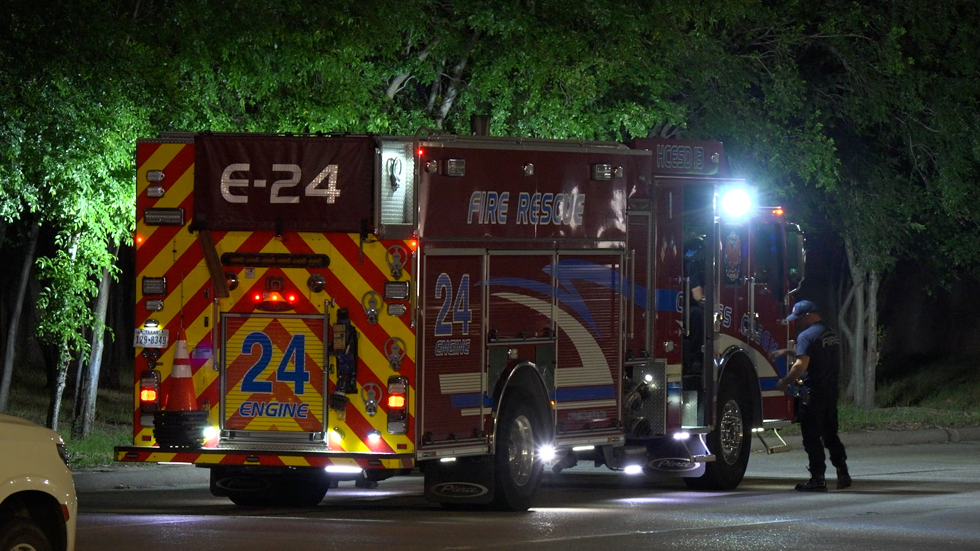Nighttime fire rescue truck labeled 24 Engine, with reflective chevrons, parked with firefighters nearby.