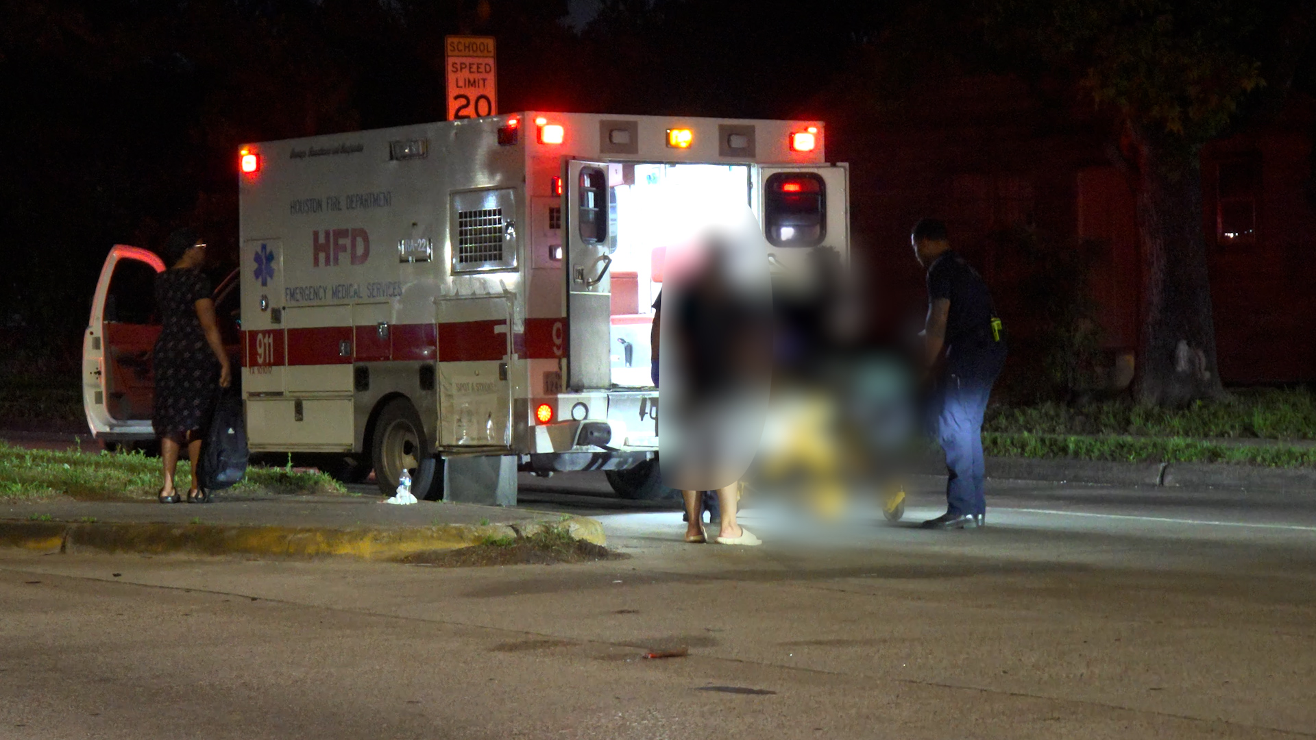 Nighttime emergency scene: a Houston Fire Department ambulance with rear doors open and responders assisting blurred figures.
