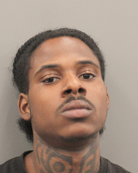 Front-facing mugshot of a young man with braids and a neck tattoo against a gray background, looking slightly upward.