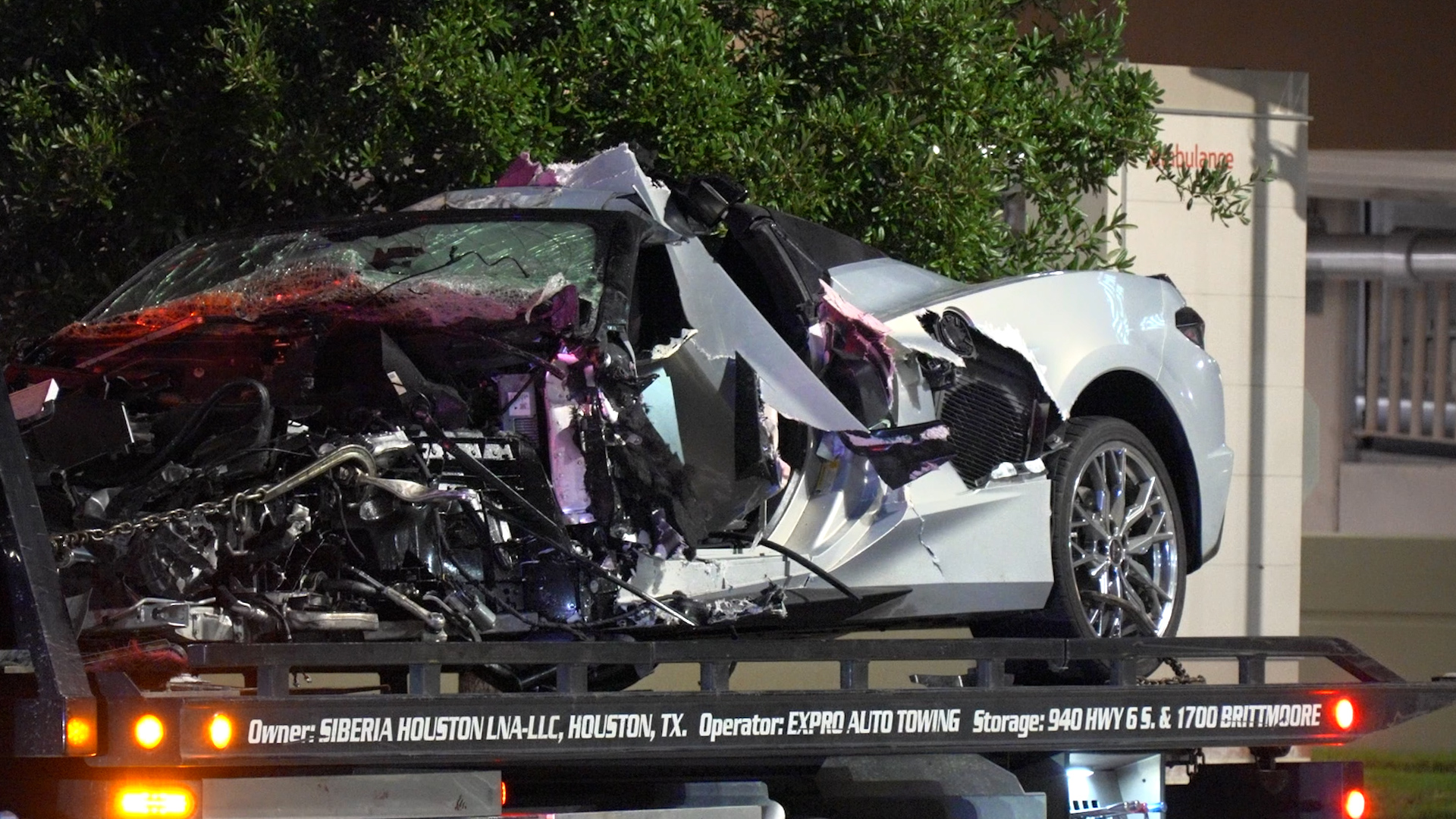 Severely damaged white sports car with a crushed front end on a tow truck bed