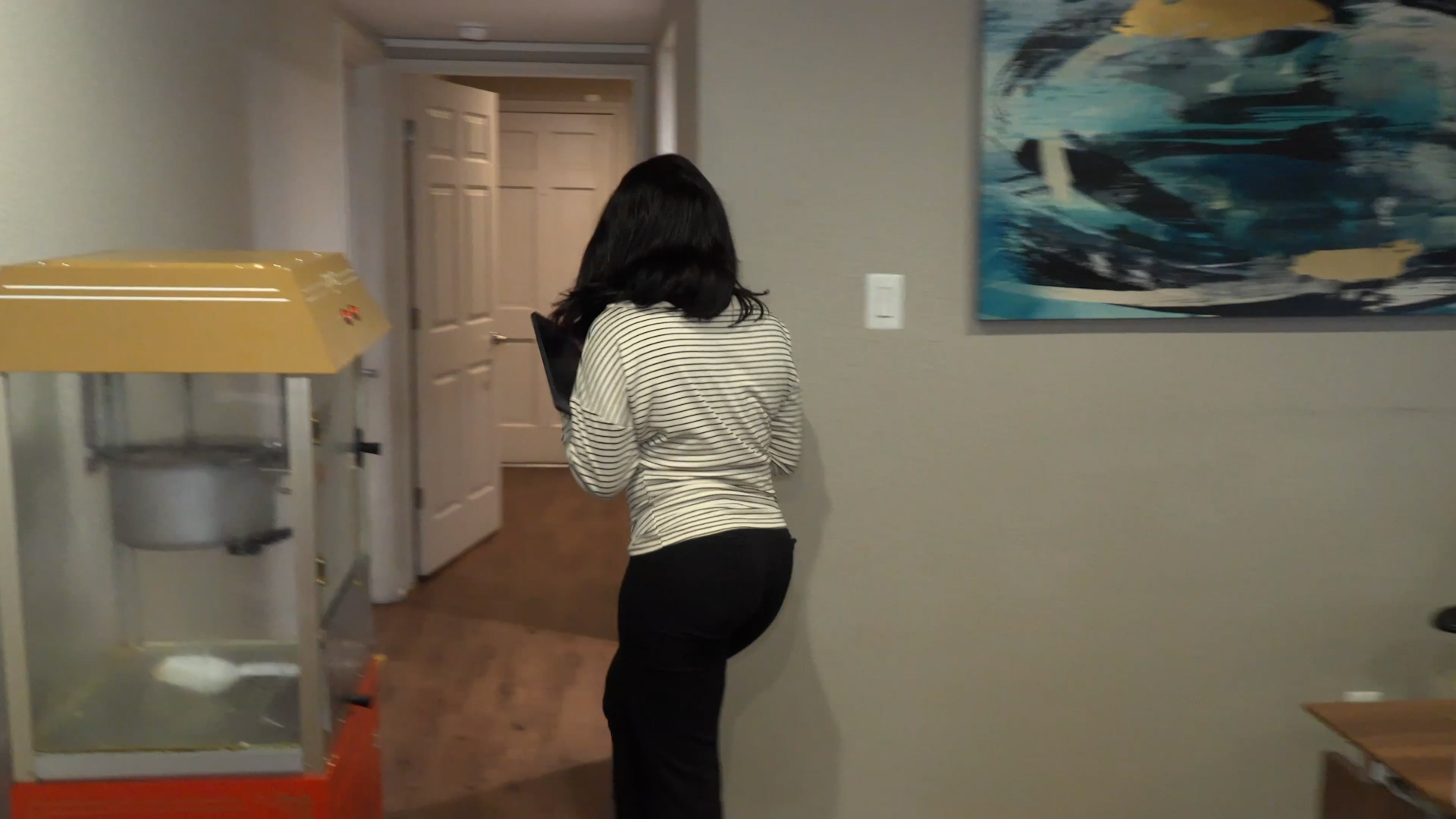 Back view of a person in a striped shirt walking down a hallway, holding a tablet.