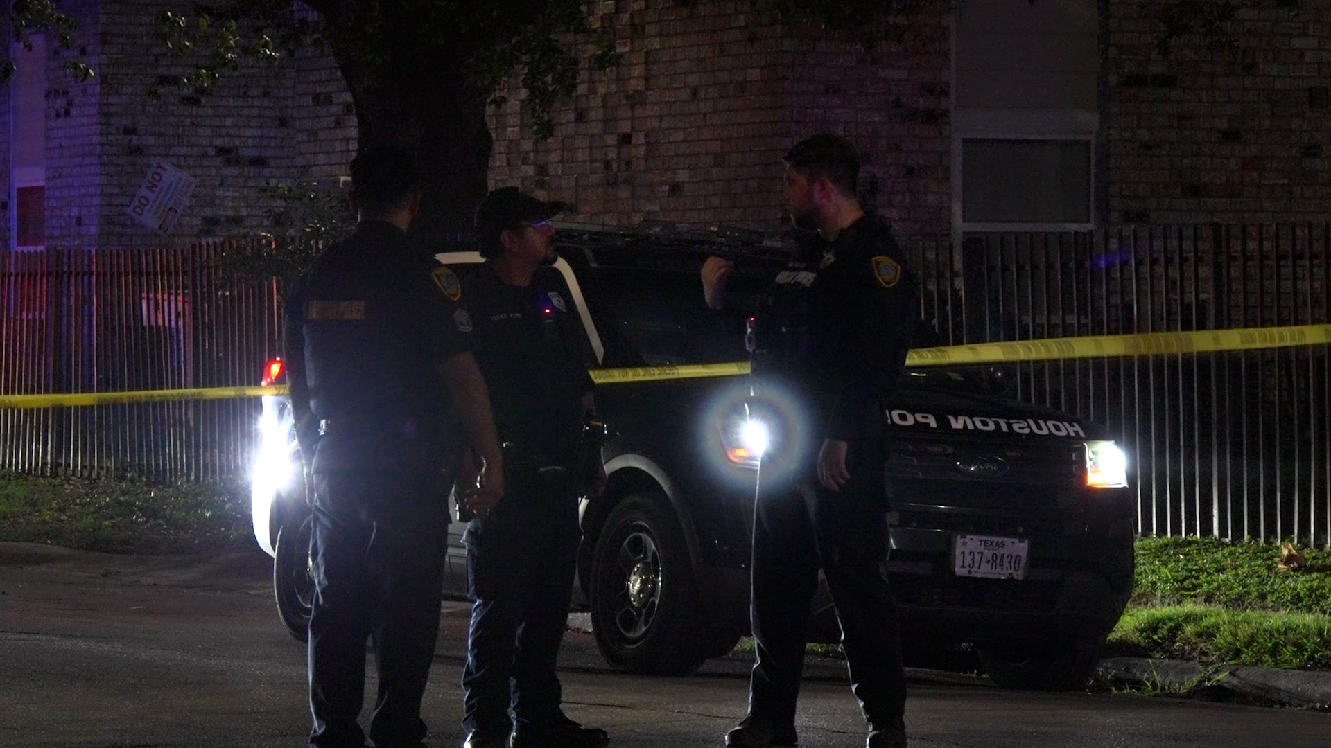 Nighttime crime scene with three police officers near a marked Houston Police SUV, beside yellow caution tape.