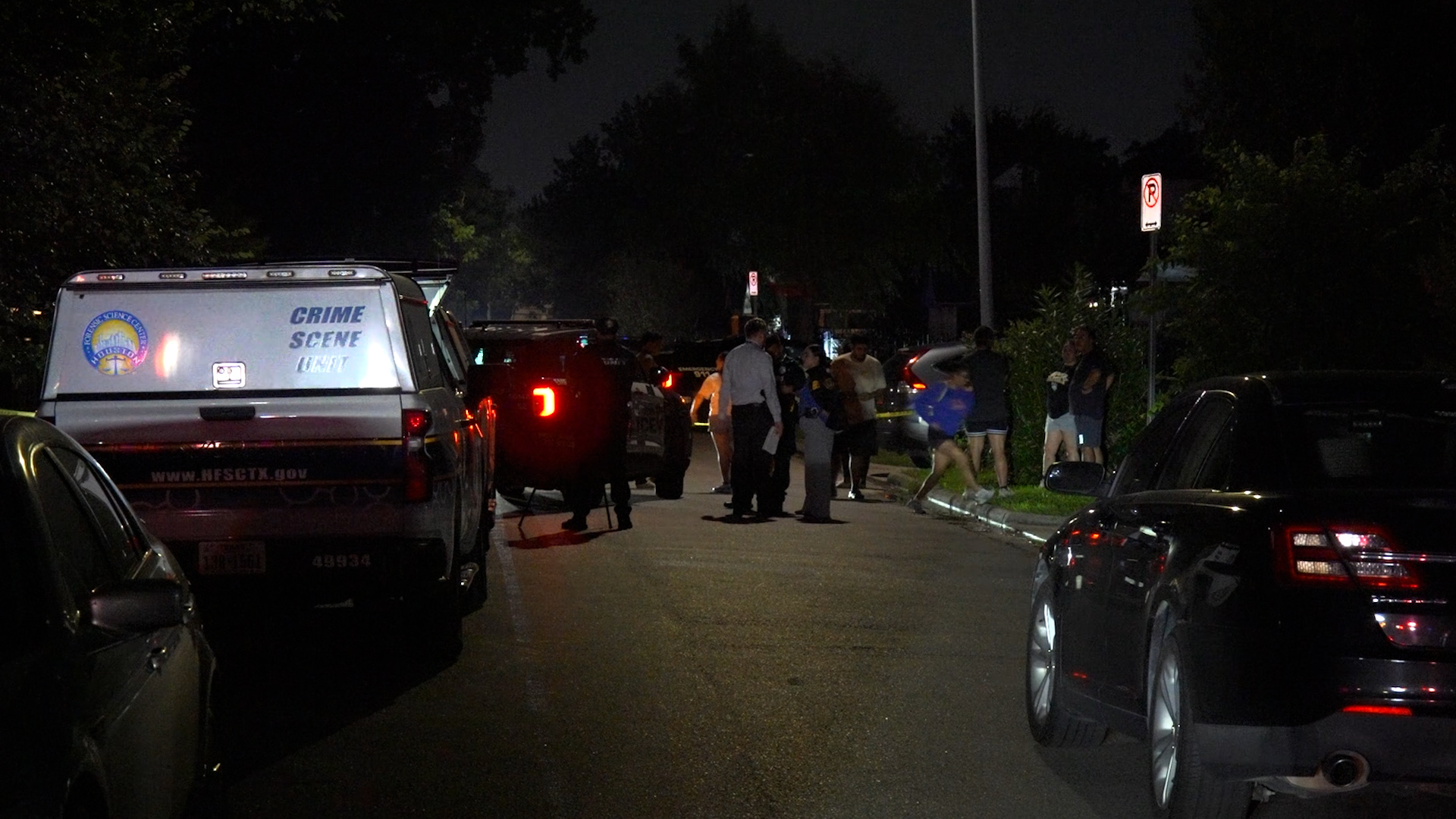 Nighttime street scene with a crime scene unit van and investigators gathered near a taped-off area on a residential street.