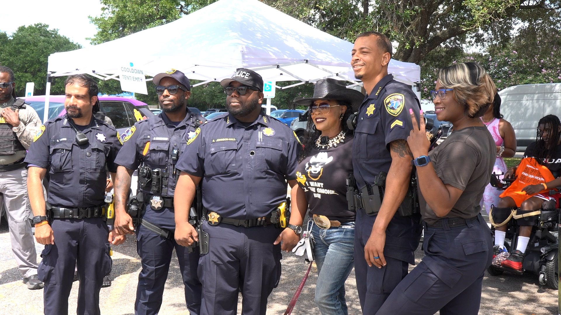 Group of diverse police officers posing for a photo at an outdoor community event under a white tent.