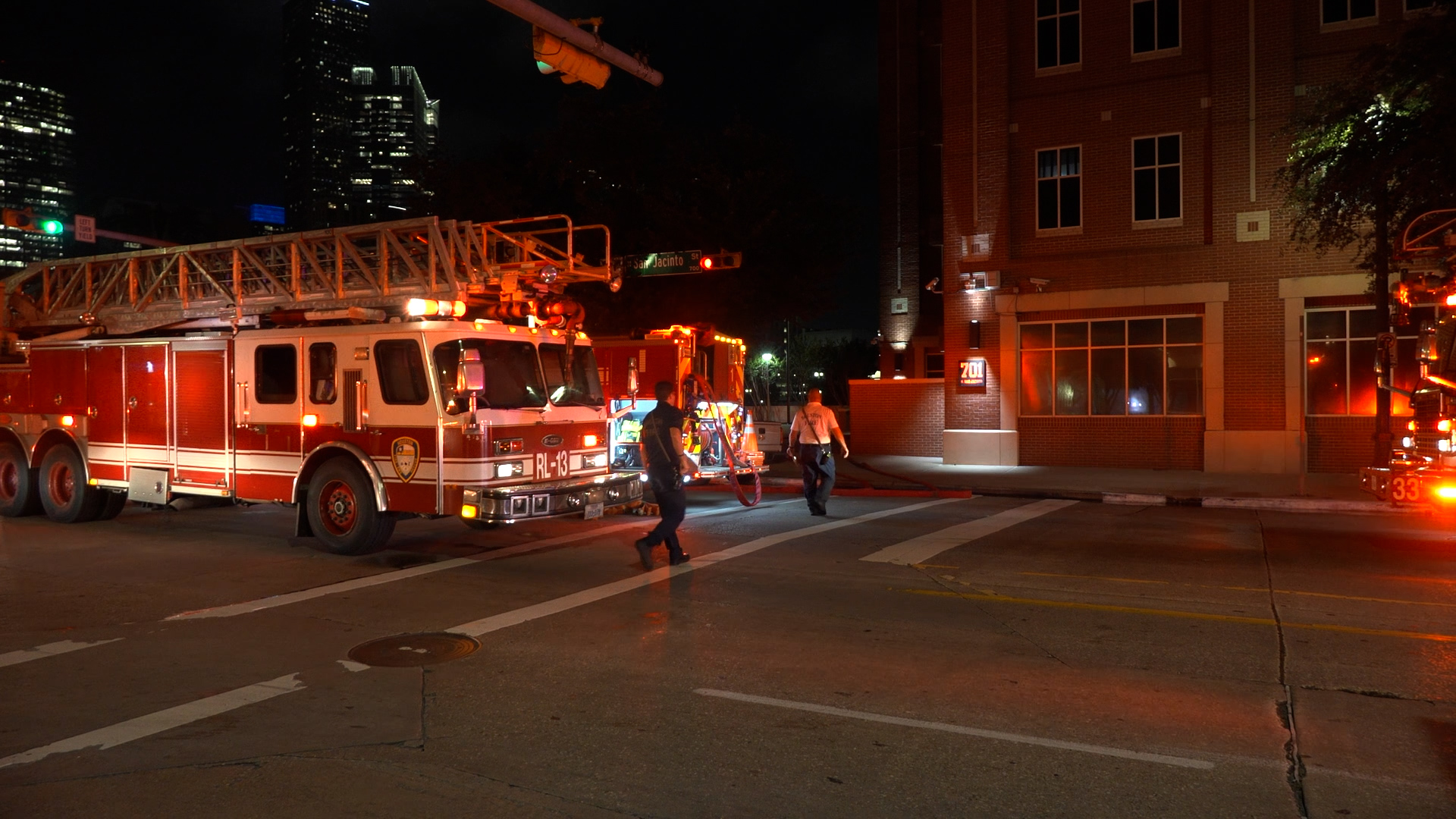 Nighttime street scene with red fire trucks and a raised ladder, firefighters working outside a brick building.