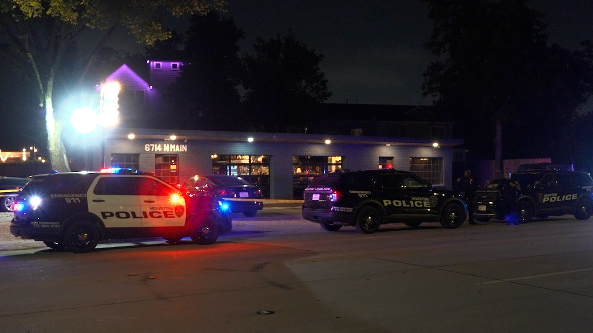 Nighttime scene with multiple Houston Police Department vehicles parked in front of a building at 6714 N Main, blue and red emergency lights flashing:
