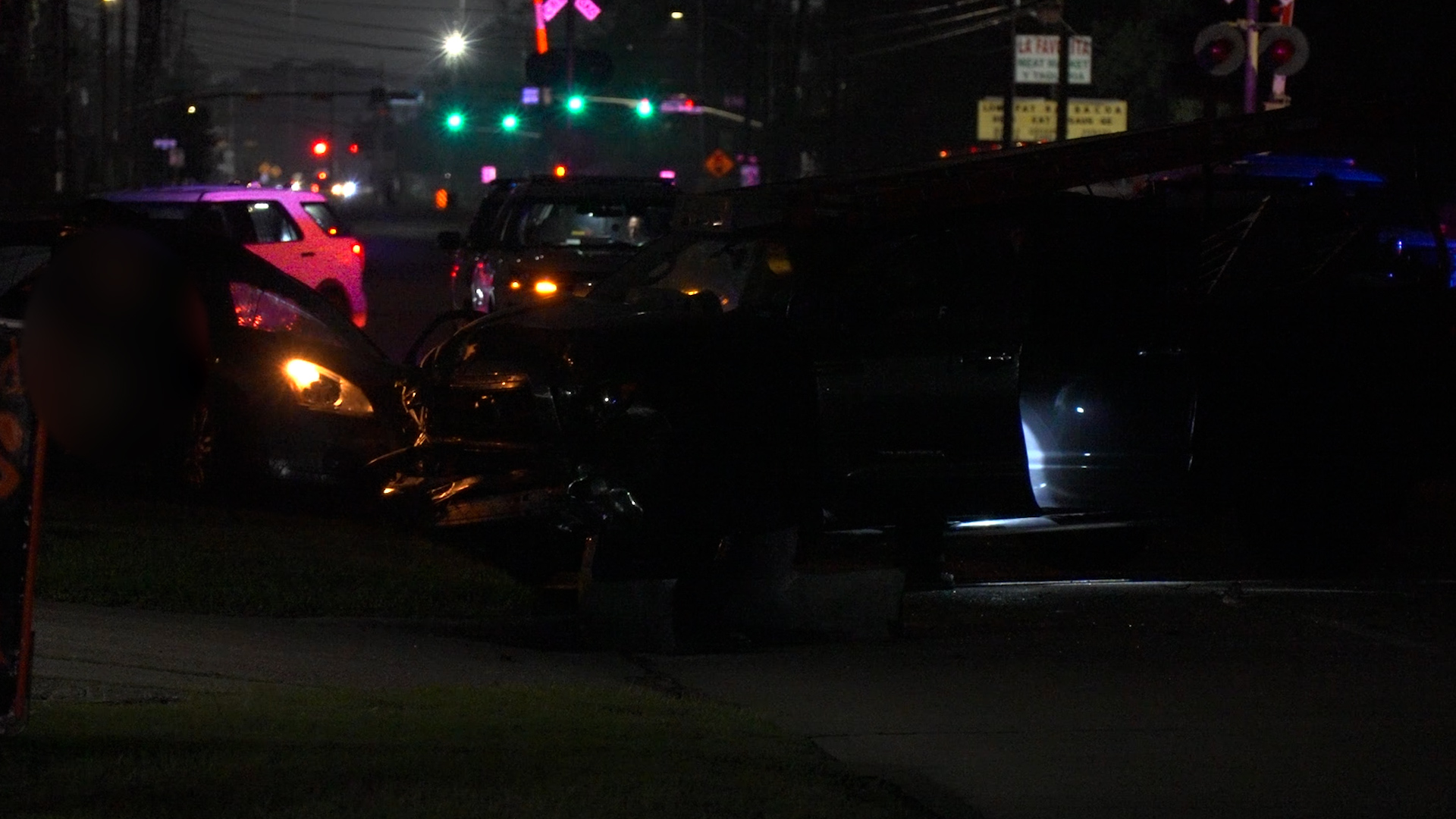 Nighttime street scene of a multi-car crash with damaged vehicles and flashing emergency lights in the background.