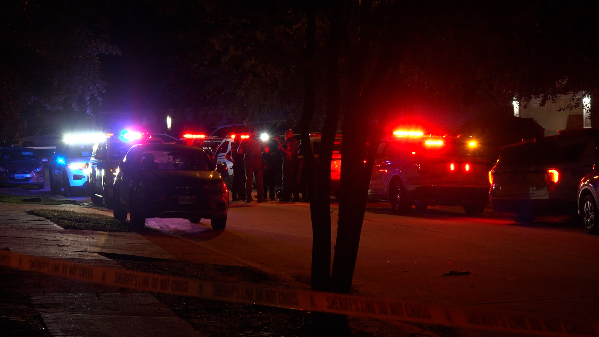 Nighttime street scene with police cars and emergency responders flashing blue and red lights.