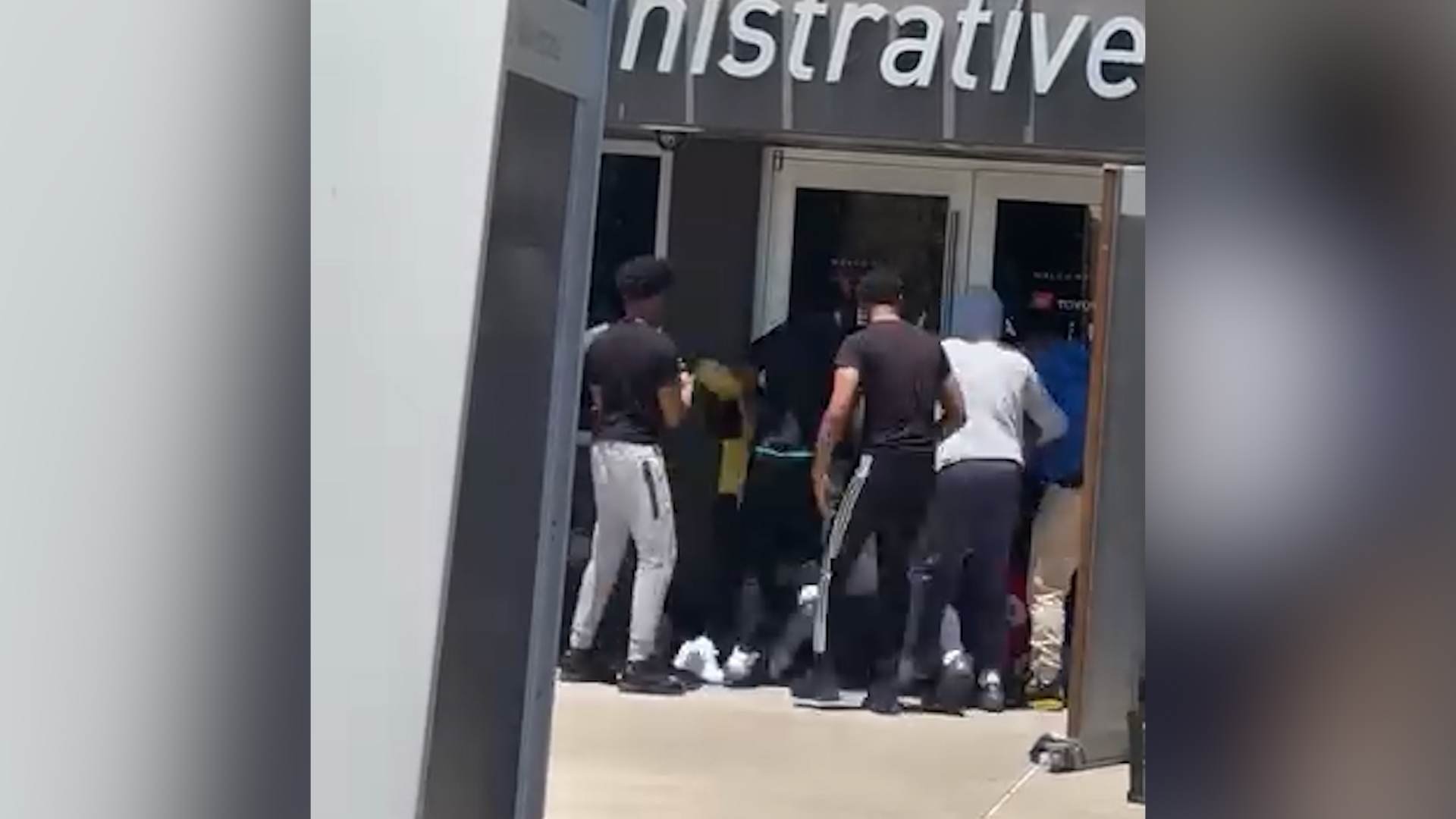 People gathered at the entrance of a storefront, some facing the glass doors as they prepare to enter.