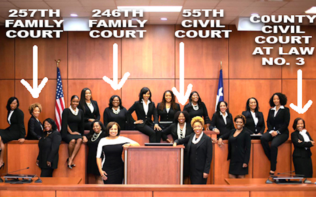 Group of women in black professional attire posing in a courthouse courtroom, with labeled court sections visible in the background.