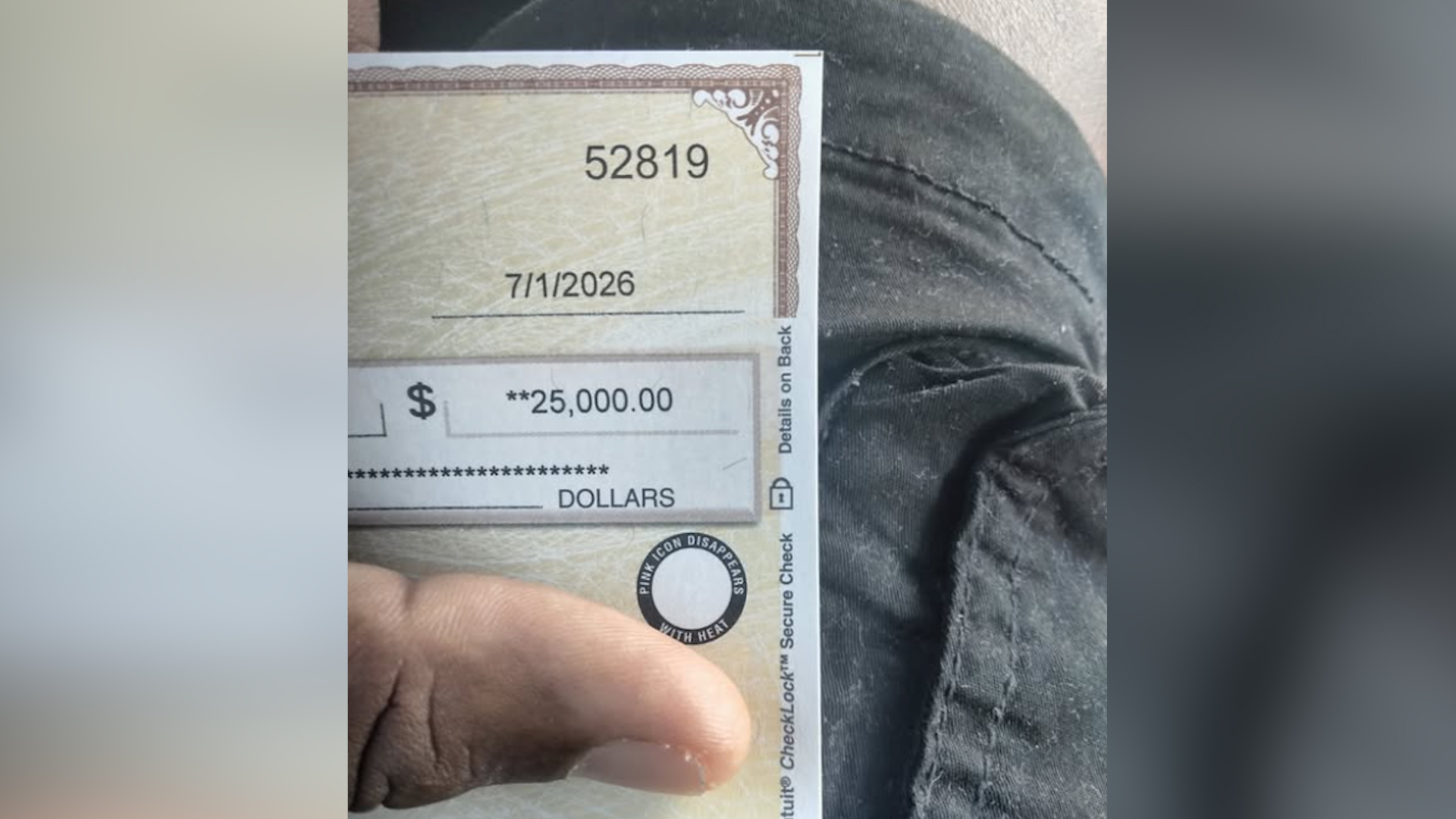 Close-up of a check showing the amount $25,000.00 and the date 7/1/2026, held by a finger.