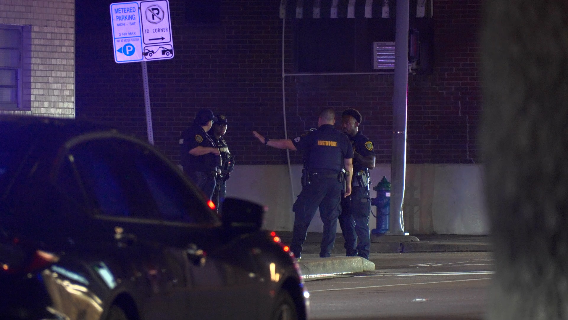 Group of Houston police officers standing and talking on a dimly lit street at night near a brick building.