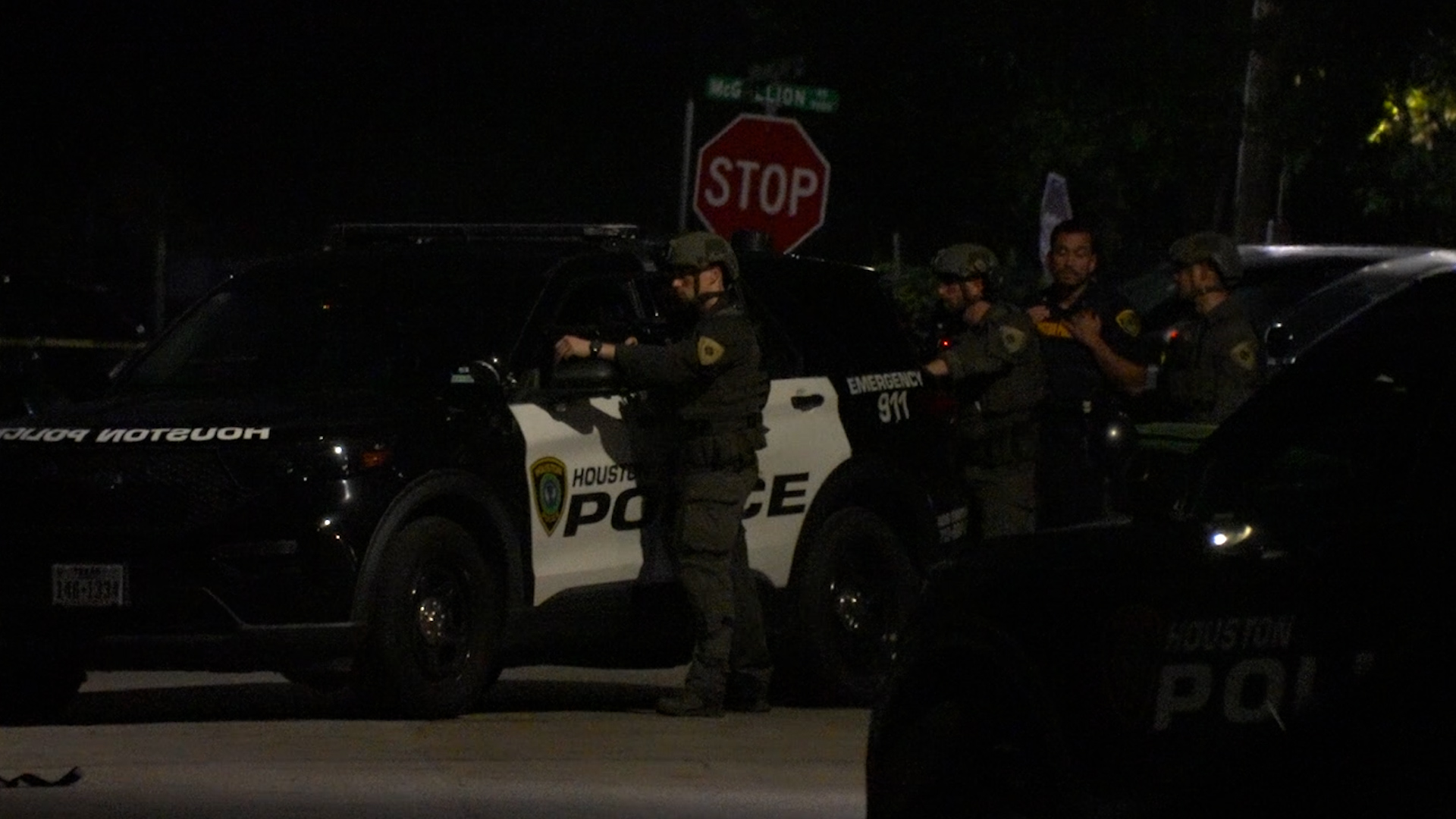 Nighttime scene with a Houston Police SUV and several armed officers in tactical gear near a stop sign.
