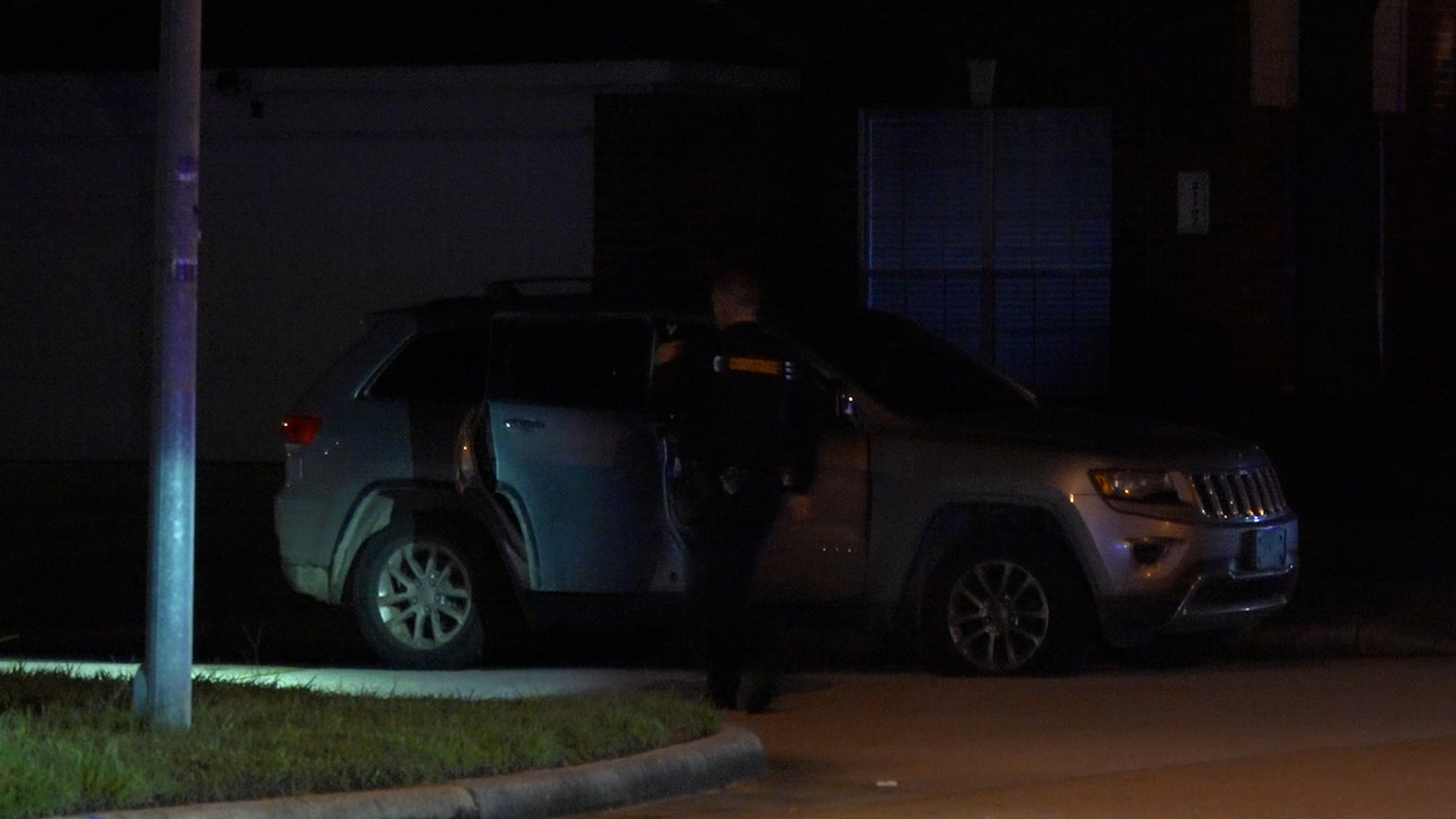 Night scene of an SUV with its rear hatch open and a police officer standing beside it in a dim parking lot.