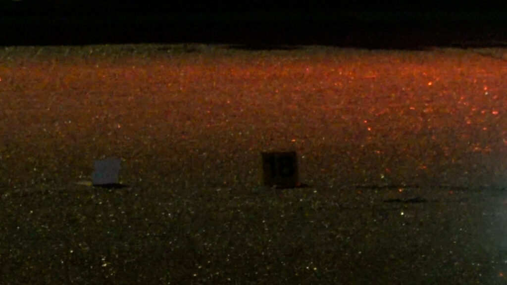 Nighttime street scene with wet pavement reflecting red light and two small square objects on the road, one white and one dark.