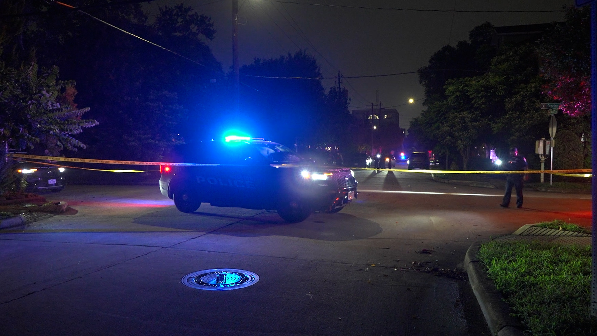 Nighttime street scene with police cars and yellow caution tape blocking a roadway.