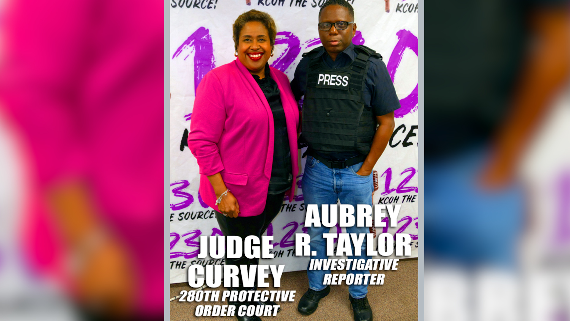 Two people posing in front of a backdrop; a smiling woman in a pink jacket and a man in a black press vest.