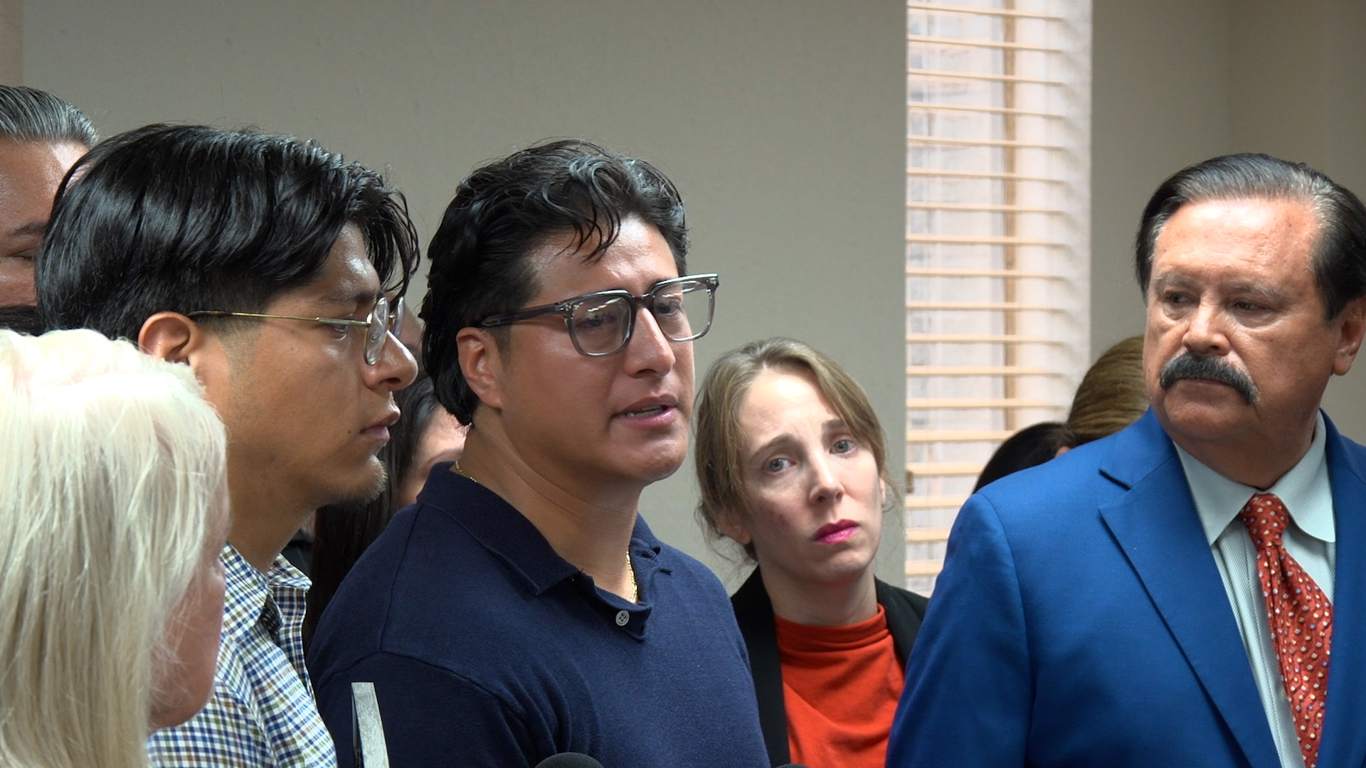 Group of adults in a crowd indoors, listening to someone speak at a briefing or meeting.