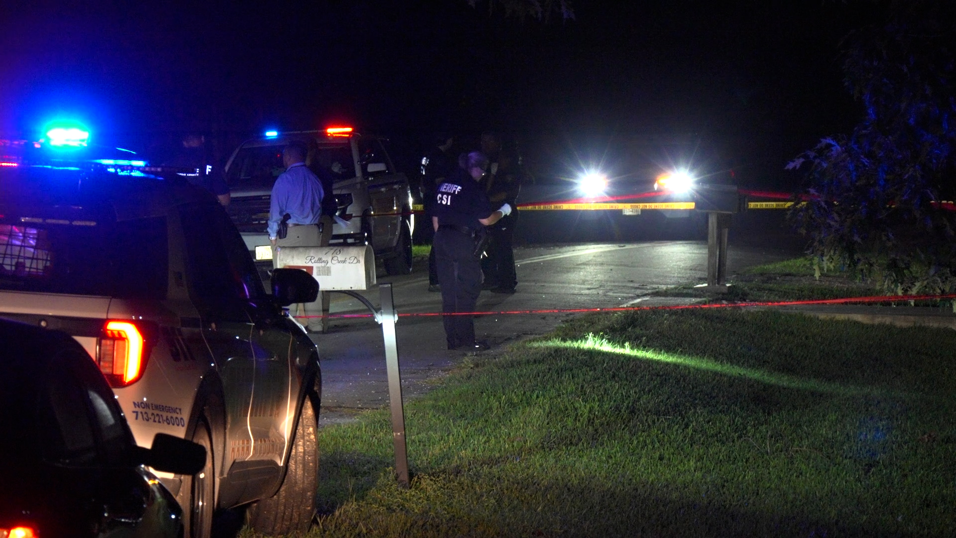Nighttime police scene with patrol cars, officers, and bright blue and red lights; yellow tape cords off the street at the scene.