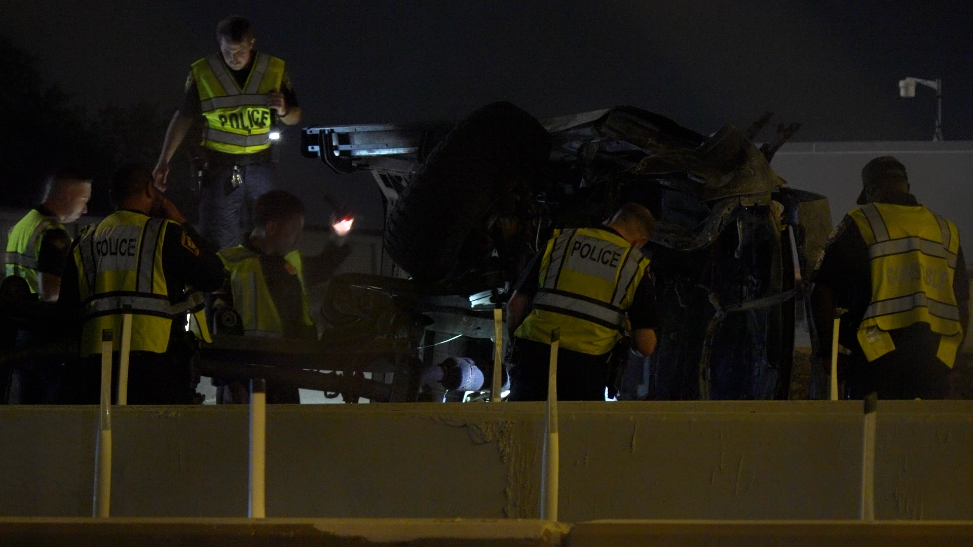 Night scene of police officers in high-visibility vests inspecting a damaged vehicle on a dark highway at night