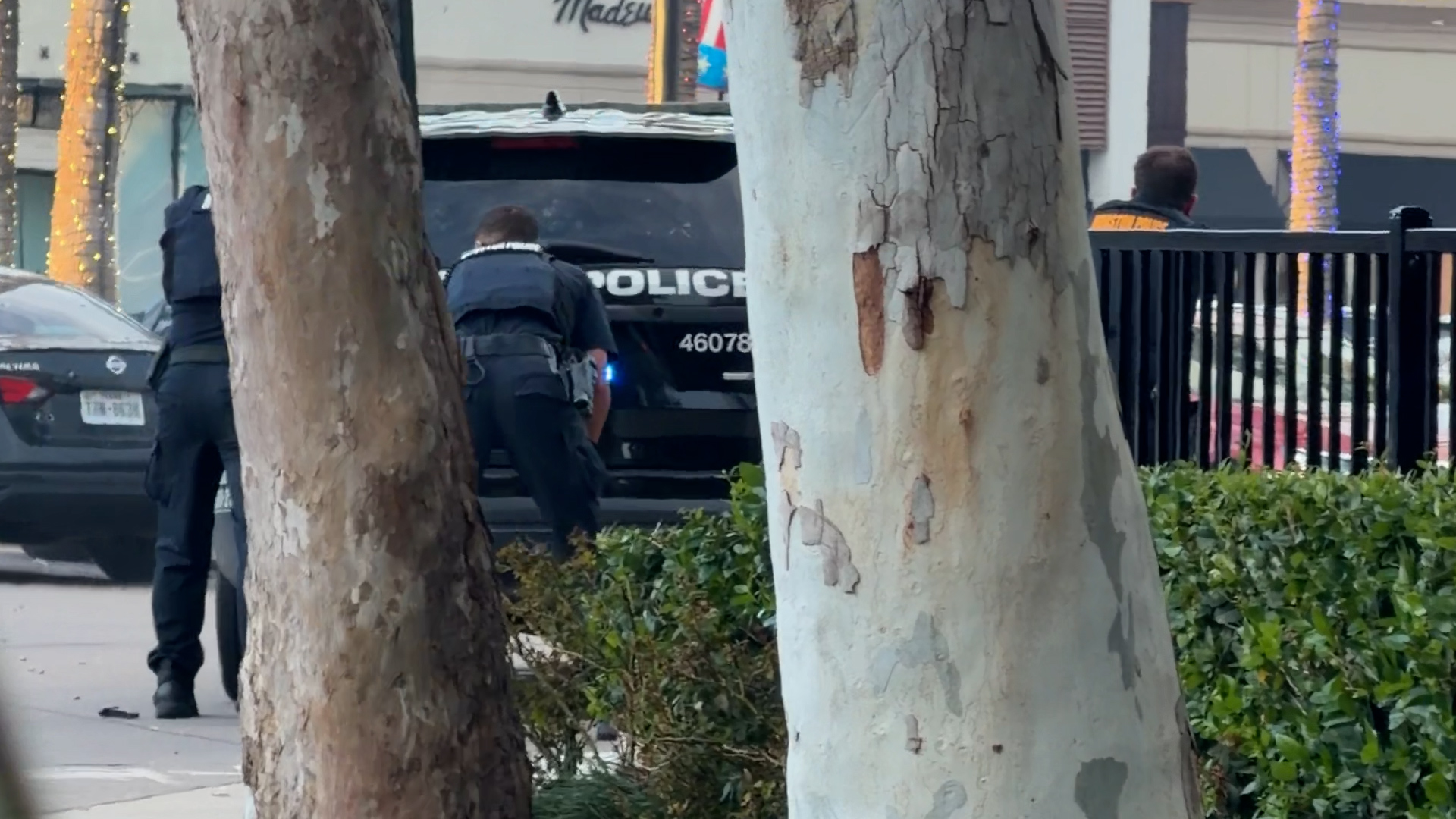 Two police officers approach a dark police SUV parked on a sidewalk, with a large 'POLICE' label visible on the rear window.