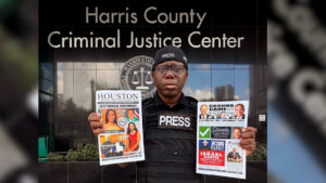 Male journalist in a PRESS vest holds two newspapers outside the Harris County Criminal Justice Center.